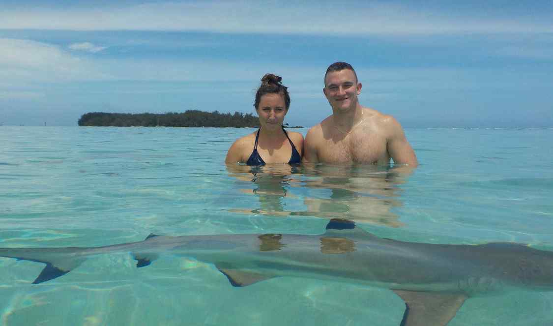 couple posant pour la photo dans le lagon devant un requin à Moorea